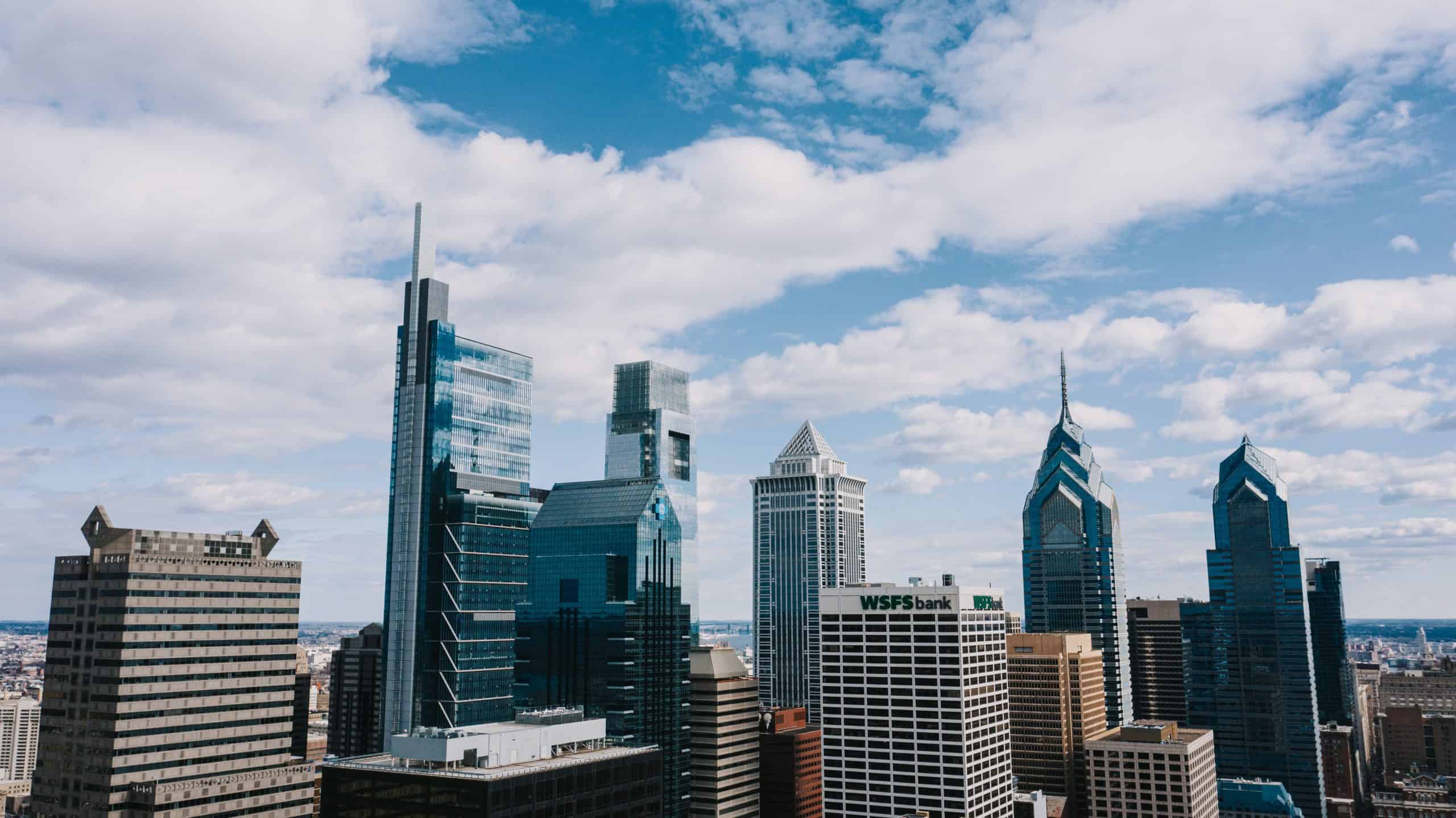 City skyline featuring tall glass skyscrapers under a partly cloudy sky.