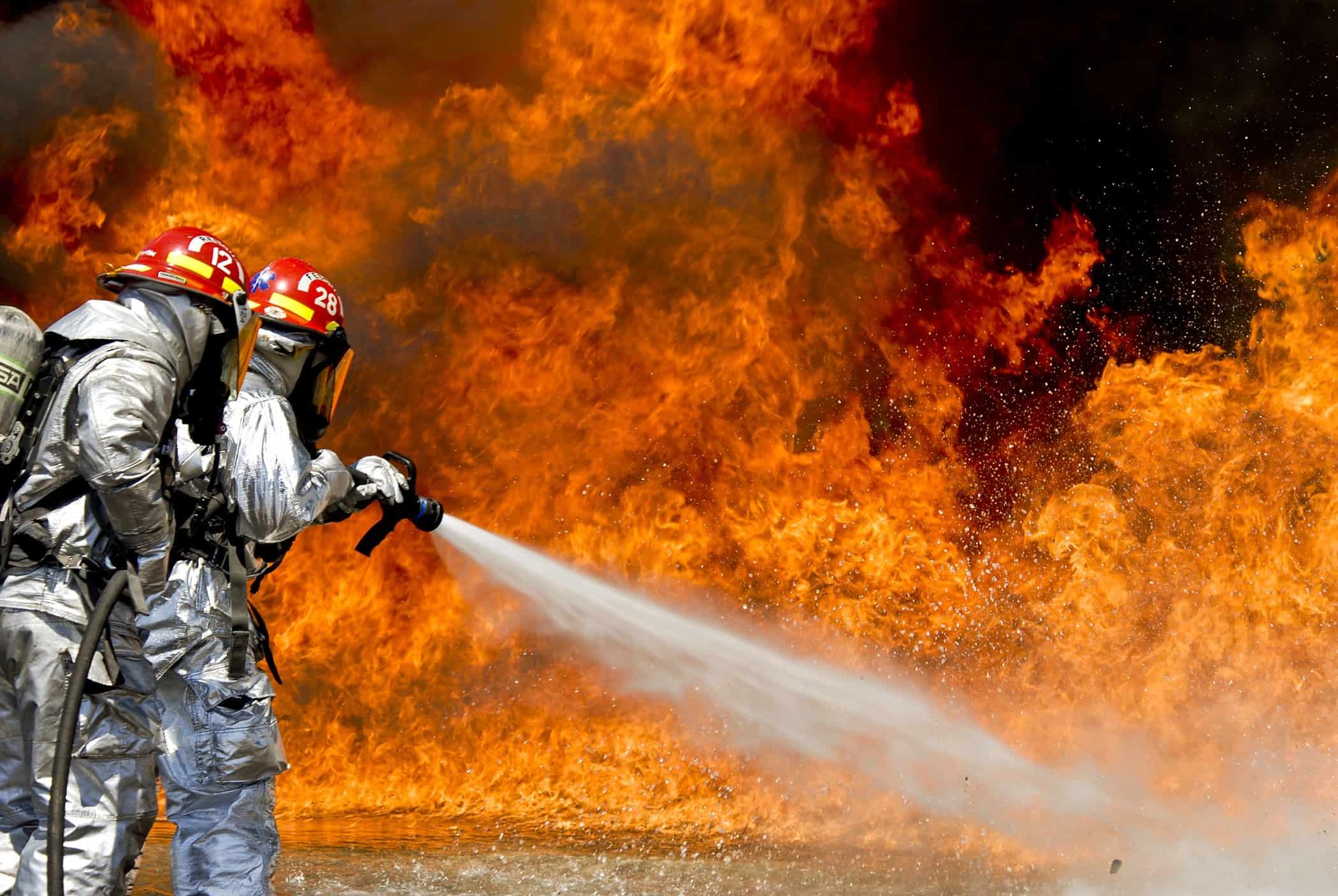 Firefighters spraying water on a massive fire with flames and smoke.